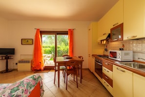 A kitchen with a dining table, chairs, a TV, and a window with curtains.
