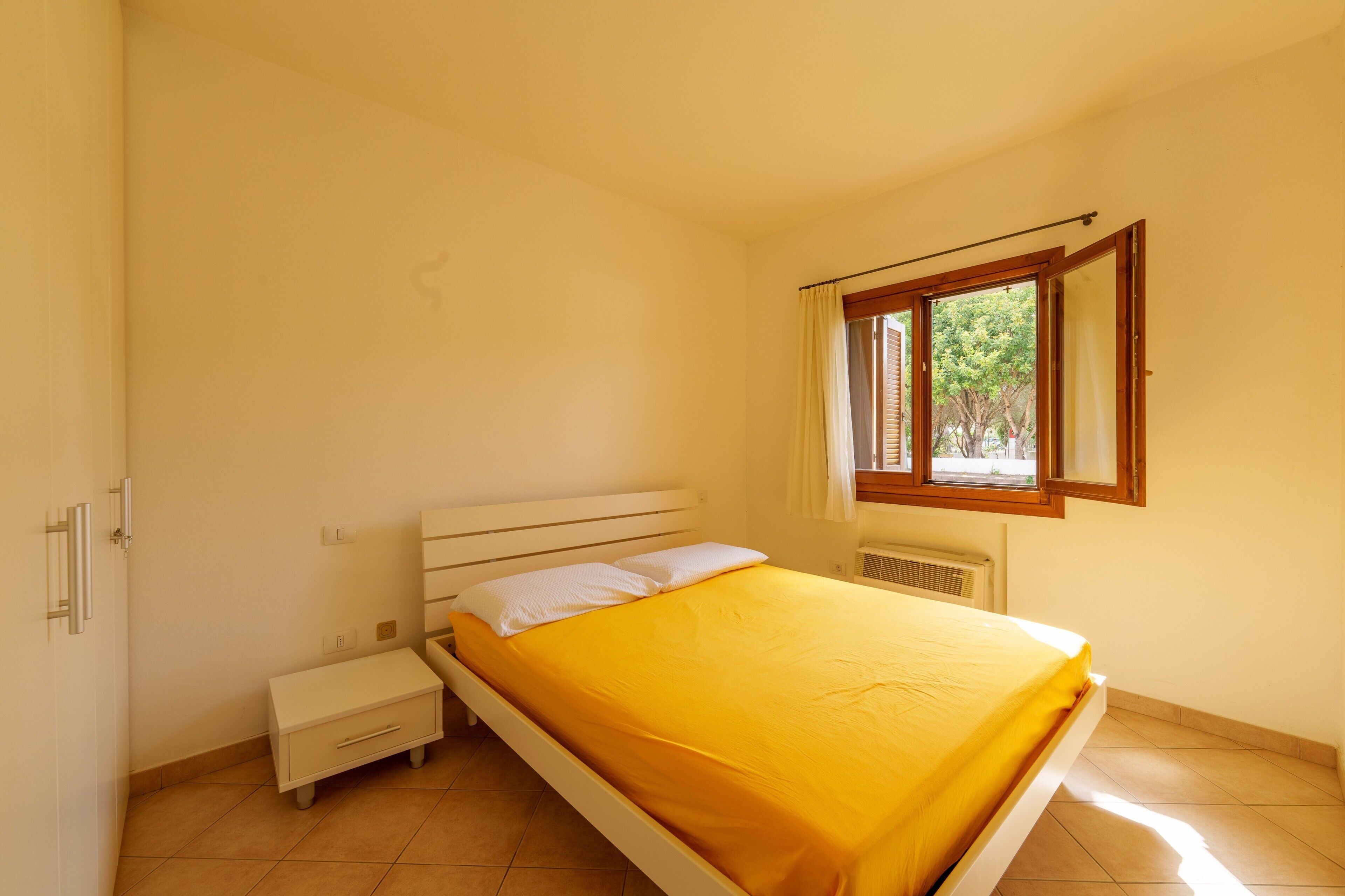 Une chambre à coucher avec un lit, une table de chevet, une fenêtre avec des rideaux et un radiateur.