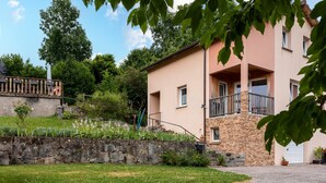 A two-story building with a stone facade, a balcony, and a stone wall with plants. - La Sabaudia Gîte in the Vosges – Up to 10 Guests (Gérardmer)