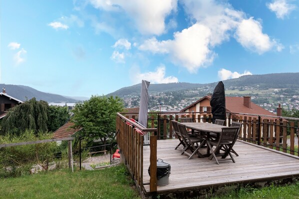 A wooden deck with outdoor furniture, a grill, and a scenic view of a town and mountains.
