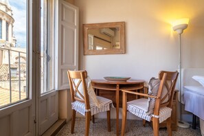Una habitación con una mesa de comedor, dos sillas, un espejo, una lámpara y vistas a un edificio a través de una ventana.