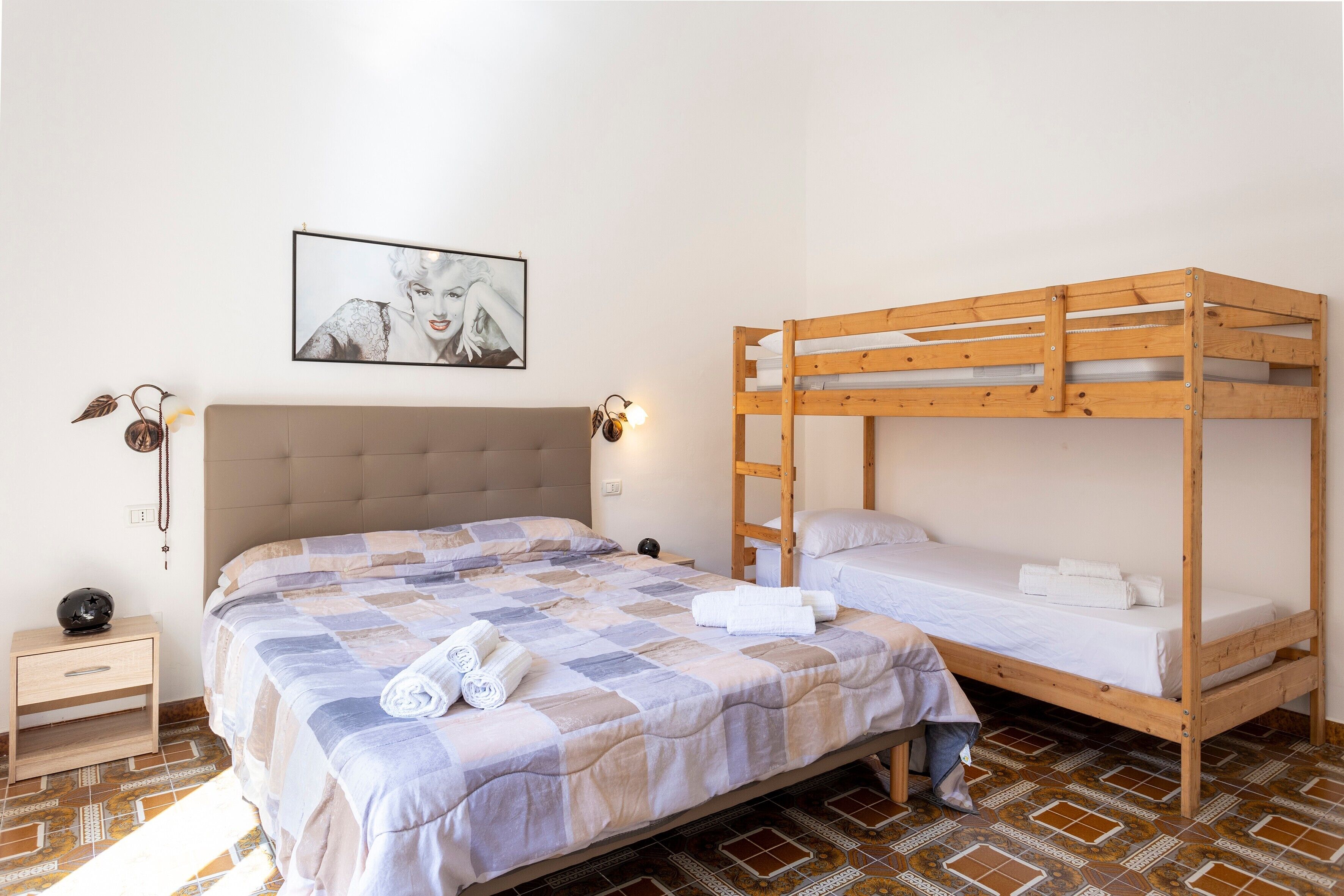 Ein Schlafzimmer mit einem großen Bett, einem Einzelbett, einem Nachttisch mit Lampe und einem gerahmten Bild an der Wand.