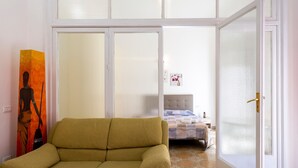 Ein Zimmer mit einer Couch, einem Bett mit blauer und weißer Bettdecke, einem Bild an der Wand und einem gefliesten Boden.
