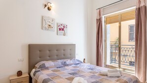 Ein Schlafzimmer mit einem Bett, einem Nachttisch, einer Wandlampe und einem Fenster mit Vorhängen.