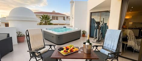 A balcony with a hot tub, a table with fruit and a bottle of champagne, and a view of a building with a dome.