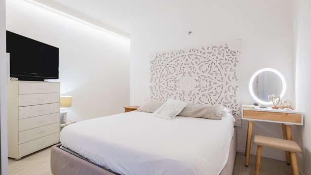 Une chambre à coucher comprenant un lit, une commode, une coiffeuse avec un miroir et un téléviseur posé sur un meuble.