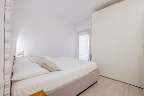 A bedroom with a bed, a wardrobe, a nightstand, and a window with blinds.