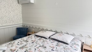 Un dormitorio con una cama, una silla azul, una mesita de noche, aire acondicionado instalado en la pared y un papel tapiz con motivos florales.