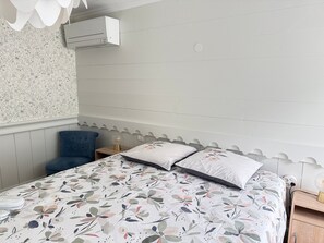 A bedroom with a bed, a blue chair, a nightstand, a wall-mounted air conditioner, and a floral-patterned wall.