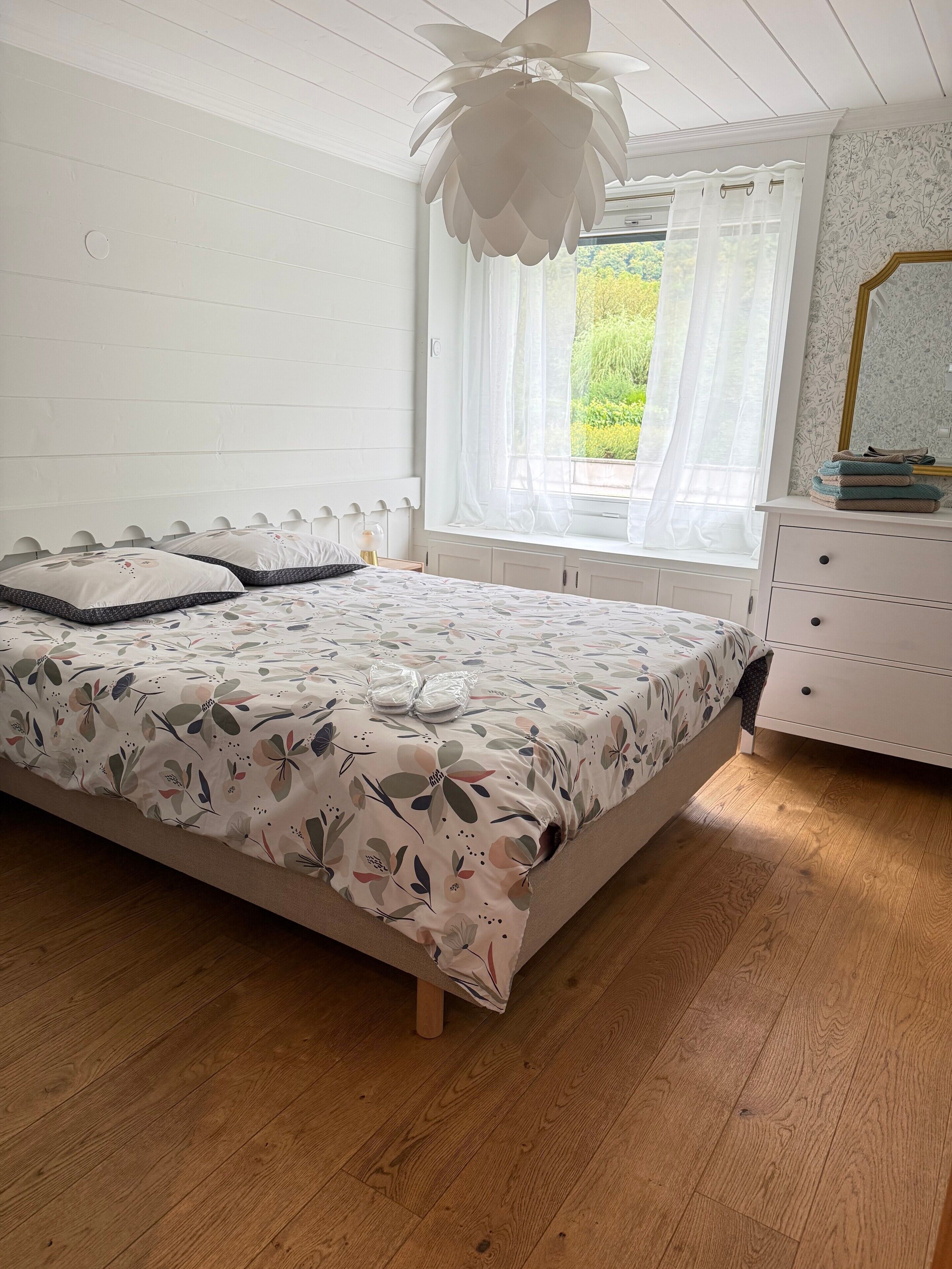 Une chambre à coucher comprenant un lit, une commode, une fenêtre avec des rideaux et un luminaire au plafond.