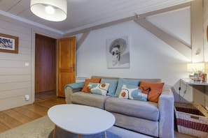 Un salon comprenant un canapé, une table ronde, une porte en bois et une œuvre d’art accrochée au mur.