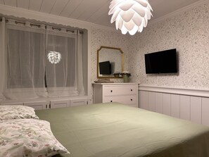 Une chambre à coucher avec un lit, une commode, un miroir et un téléviseur fixé au mur.