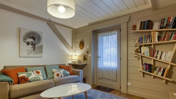 A living room with a sofa, a coffee table, a bookshelf, and a door with a window. - Appartement climatise au pied des cols avec wifi (La Bathie)