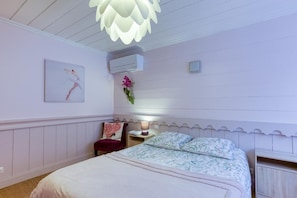 Une chambre à coucher comprenant un lit, une chaise, une table de chevet, un climatiseur fixé au mur et un luminaire décoratif.
