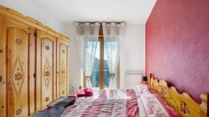 Een slaapkamer met een bed, een houten garderobe en een raam met dunne gordijnen.