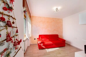 Un divano rosso in una stanza con parete chiara e finestra con tende.