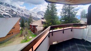 A wooden balcony with a view of snow-capped mountains and pine trees.