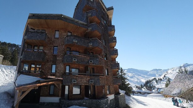A multi-story wooden building with balconies, set against a snowy mountain backdrop.