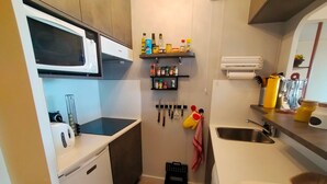 A compact kitchen with a microwave, kettle, and sink. There are shelves with spices and utensils.