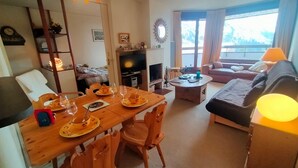 A cozy living room with a wooden dining table set for two, a sofa, and a TV.