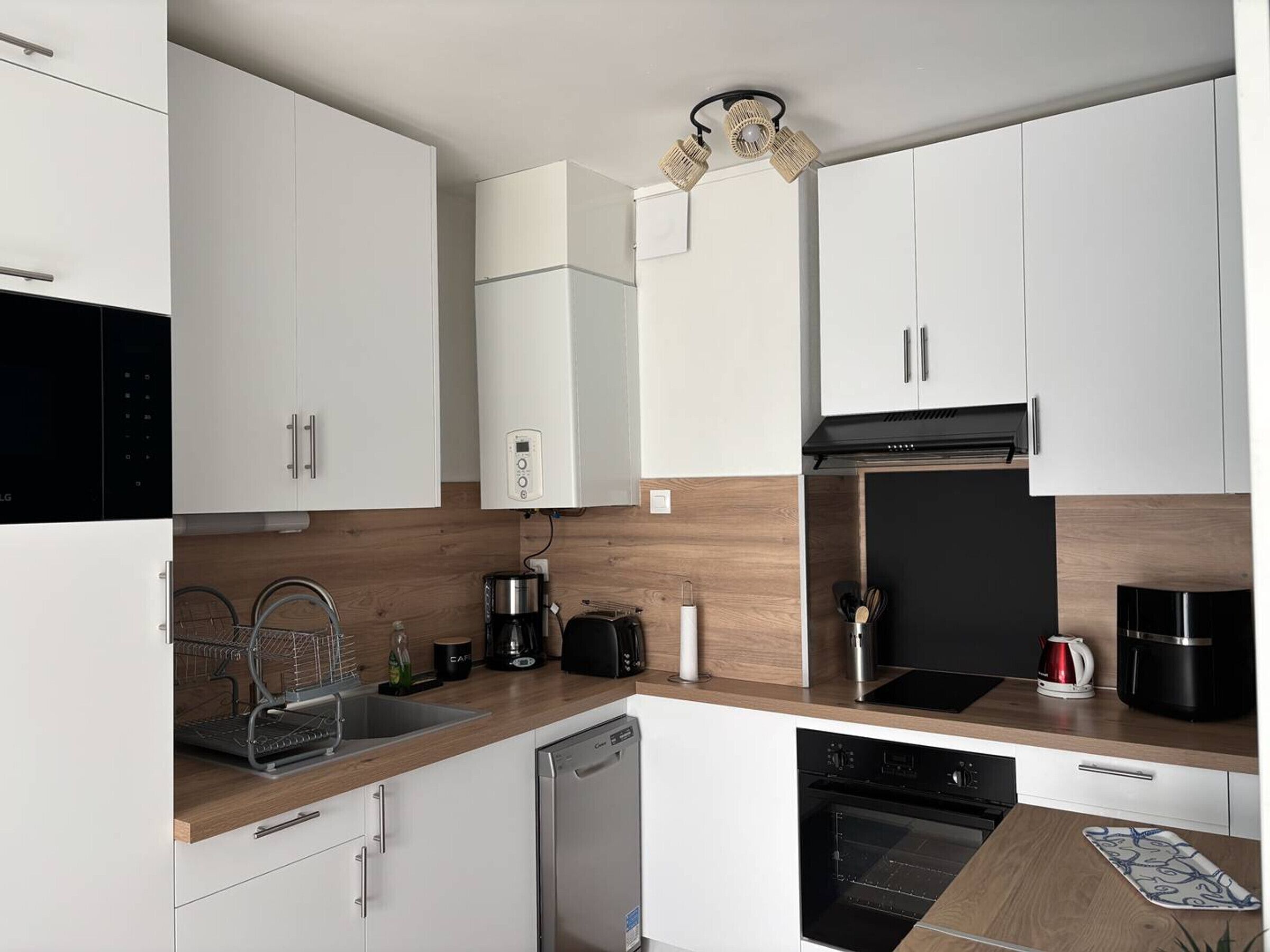 Una cocina moderna con armarios blancos, lavavajillas, horno, cafetera y hervidor.