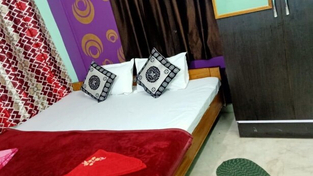 A bed with a red blanket and patterned pillows, a green mat on the floor, and a wardrobe with a mirror. - Puri (Puri)