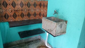 A bathroom with a turquoise wall, a patterned tile backsplash, a metal sink, and a red bucket. - Puri (Puri)