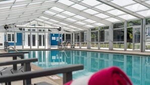 Una piscina con techo de vidrio, sillas de descanso y un letrero azul con texto.