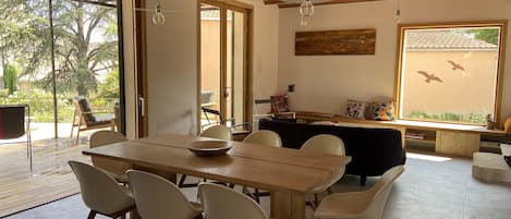 Un'ampia zona pranzo con tavolo e sedie in legno, una ventola a soffitto e vista all'esterno attraverso ampie finestre.