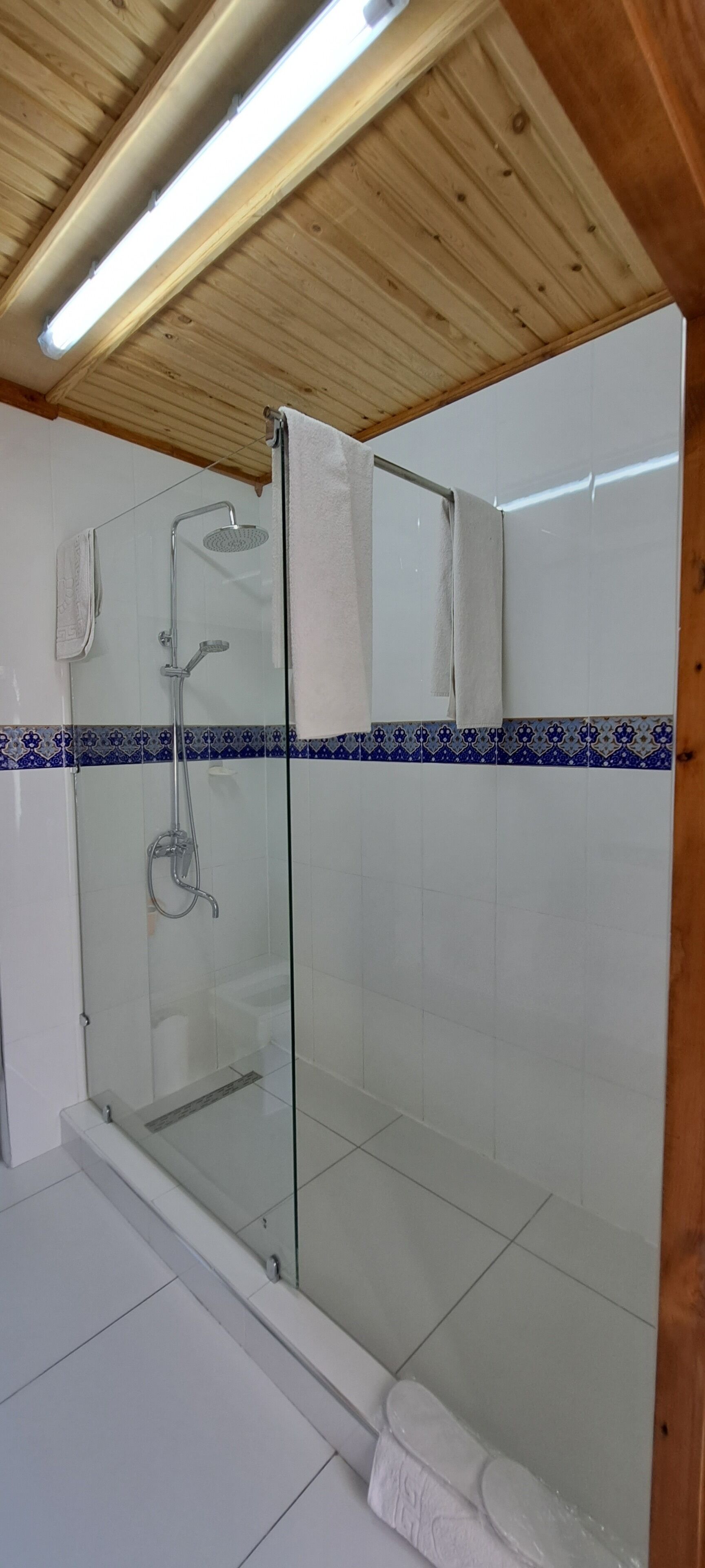 Une douche entièrementClose avec des parois en verre, un sol carrelé de carreaux blancs et un plafond en bois.