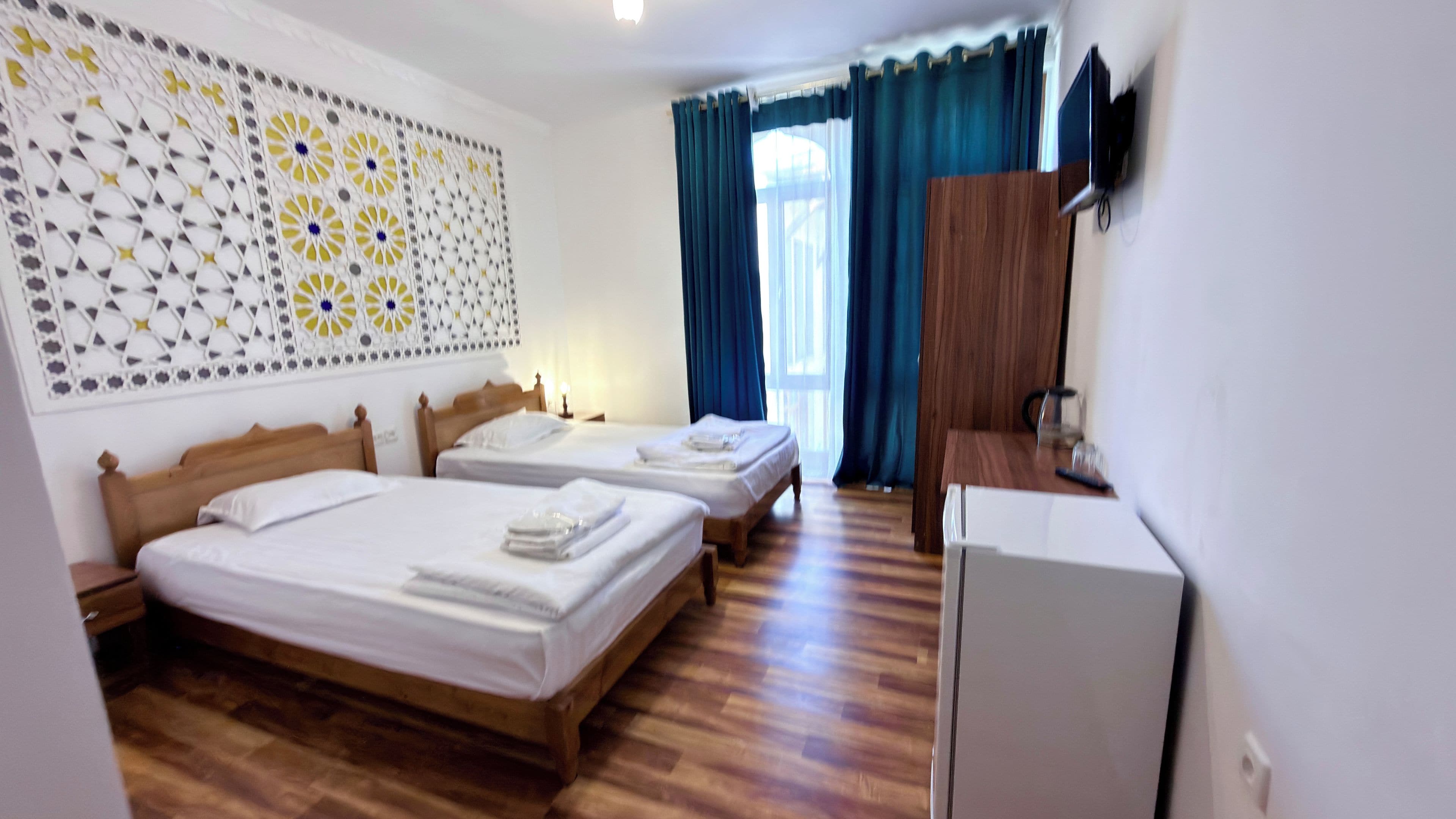 Une chambre d’hôtel avec deux lits simples, un plancher en bois, un téléviseur à écran plat et un panneau décoratif mural.