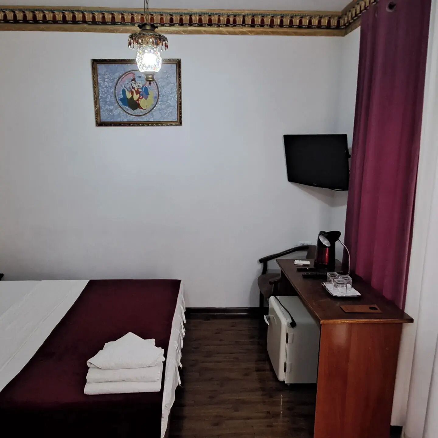 A hotel room with a bed, a desk with a computer, a television, and a decorative wall hanging.