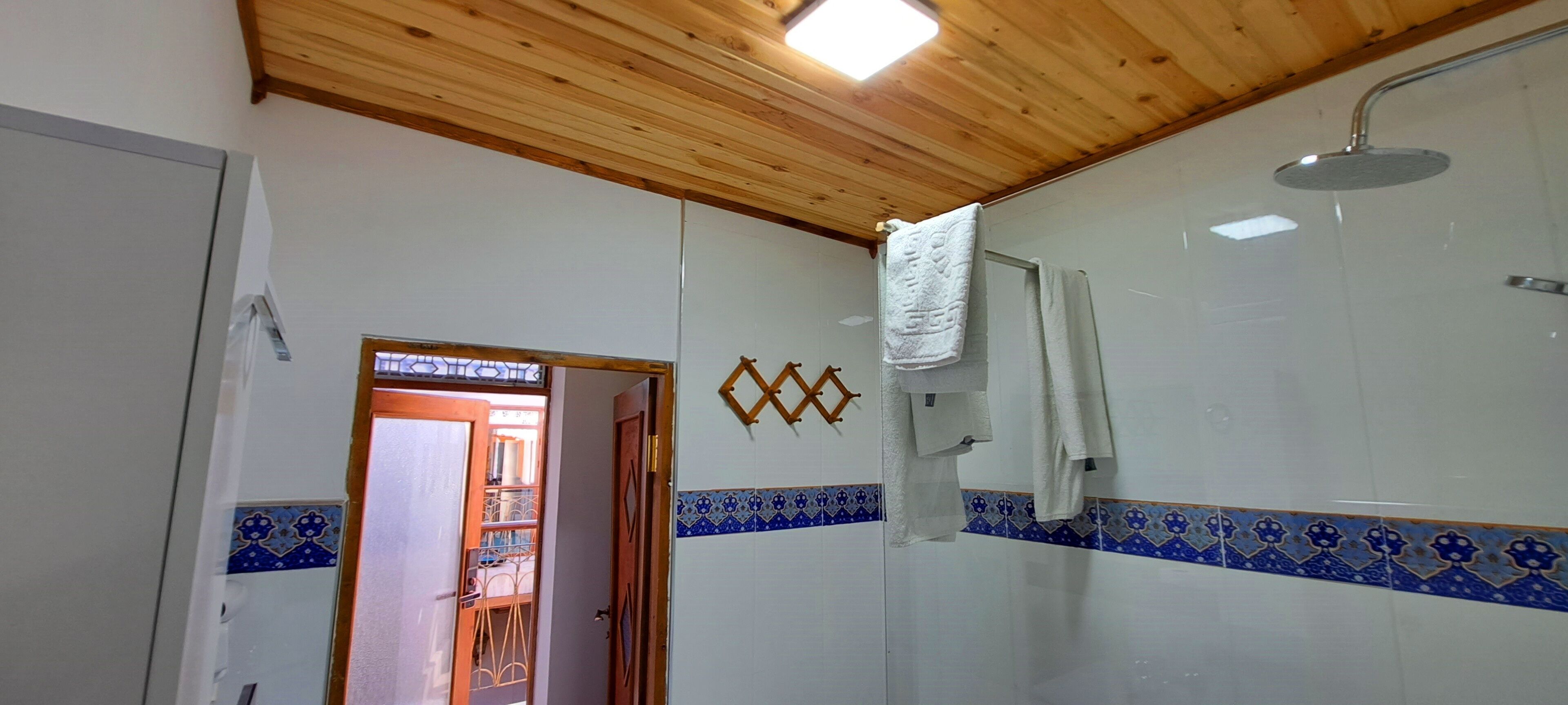 A bathroom with a wooden ceiling, a shower, and a door leading to a balcony.
