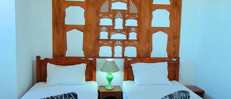 A room with two wooden beds, a wooden ceiling with a decorative pattern, and a green lamp on a nightstand.