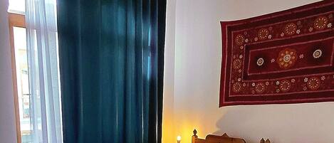 A spacious bedroom with a large bed, wooden flooring, a hanging light fixture, and a decorative tapestry on the wall.