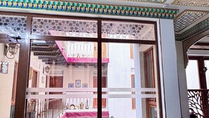A room with intricate ceiling designs, a central table with an open book, and a view of a courtyard with a staircase. - Hotel Ansi Boutique W&S terrace (Bukhara)
