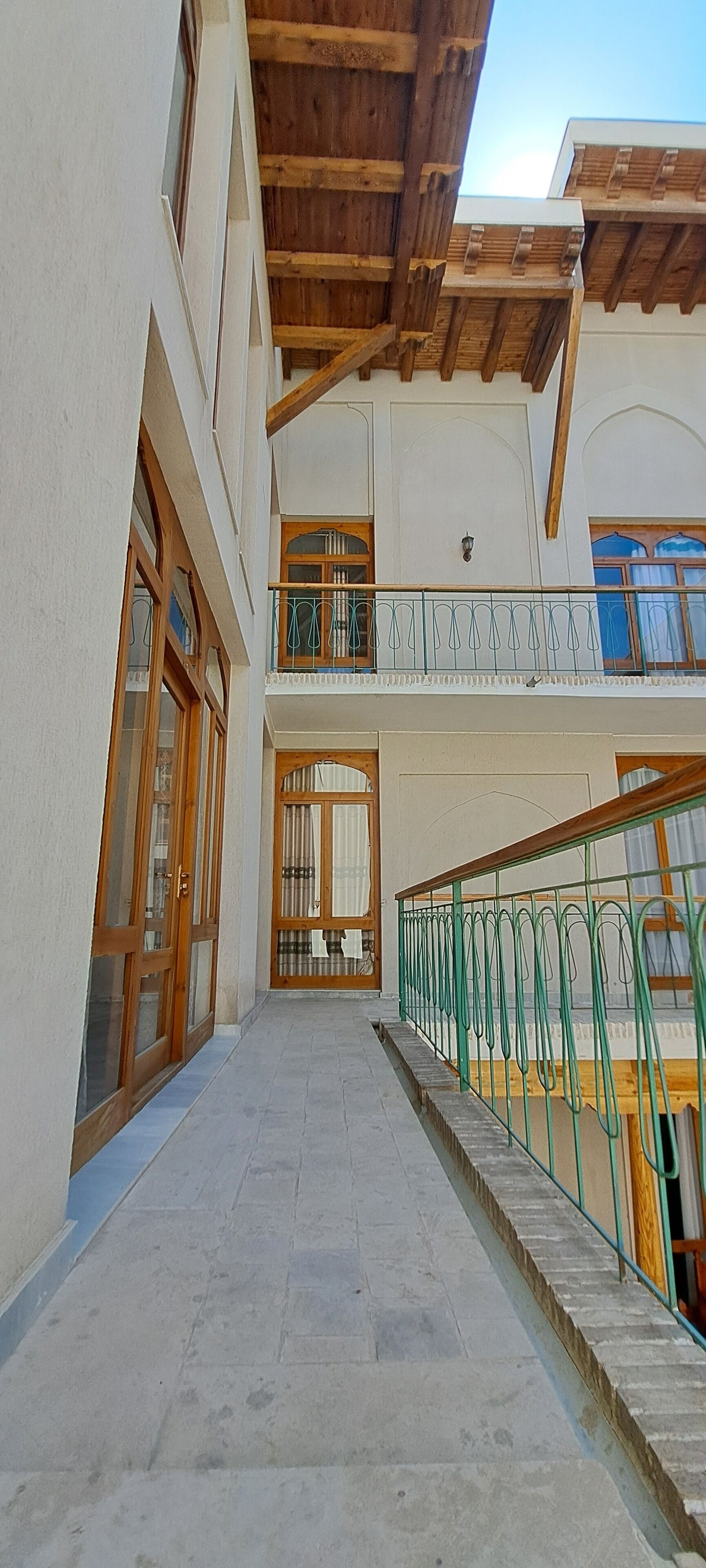 A building with a covered walkway, wooden doors, and a balcony with a green railing.