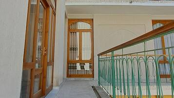 A building with a covered walkway, wooden doors, and a balcony with a green railing.