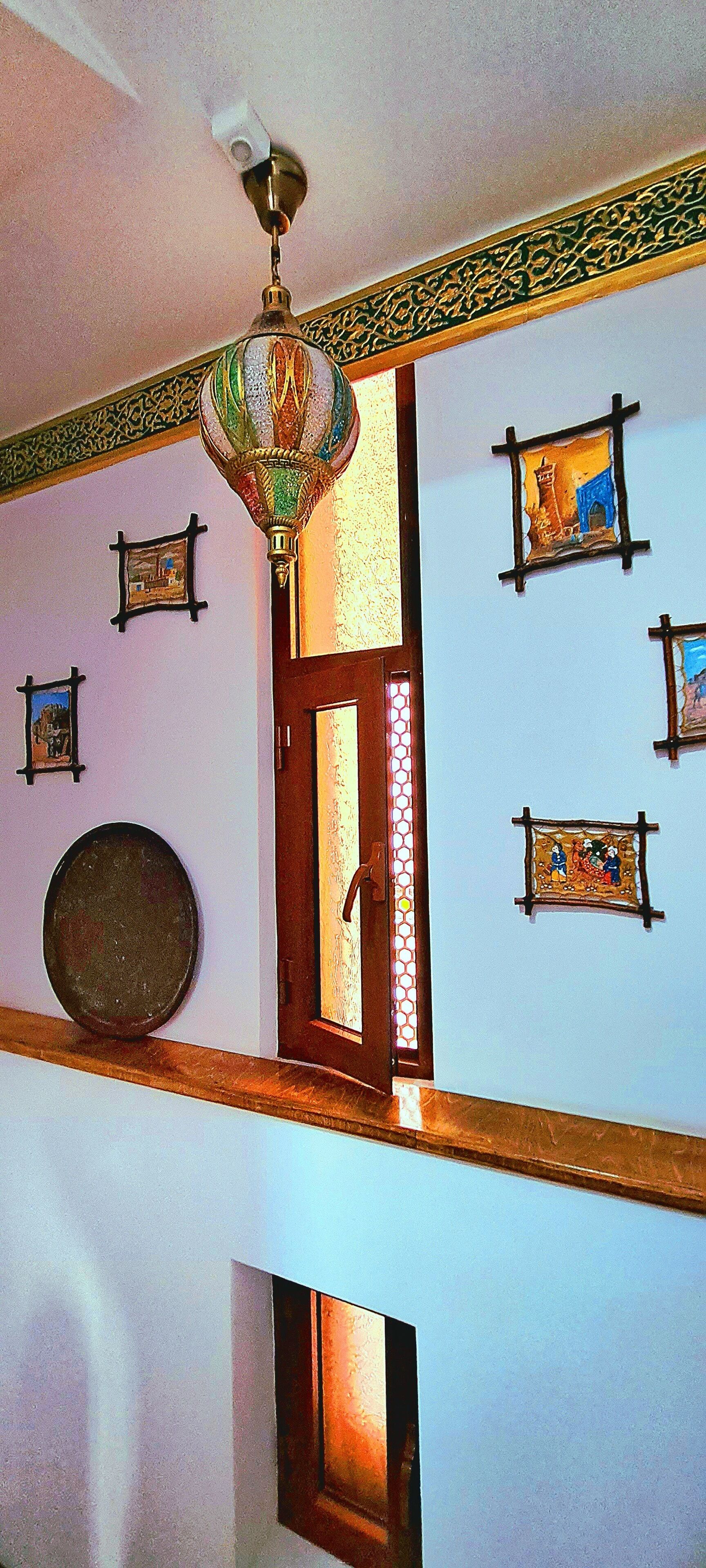 Une pièce dotée d’un lustre décoratif au plafond, d’une porte en bois ornée d’un vitrail et de plusieurs tableaux encadrés accrochés aux murs.