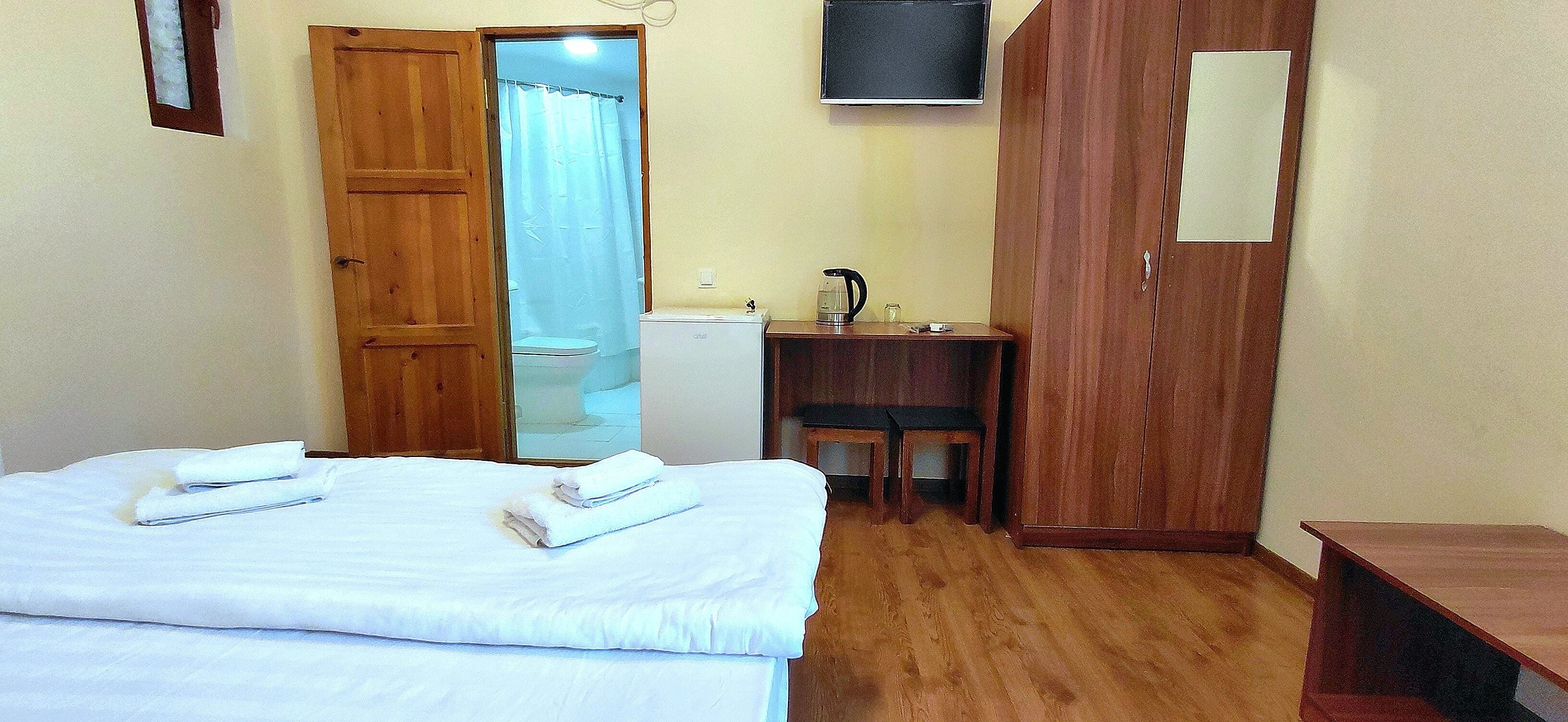 A hotel room with a bed, a desk, a chair, a wardrobe, and a television.