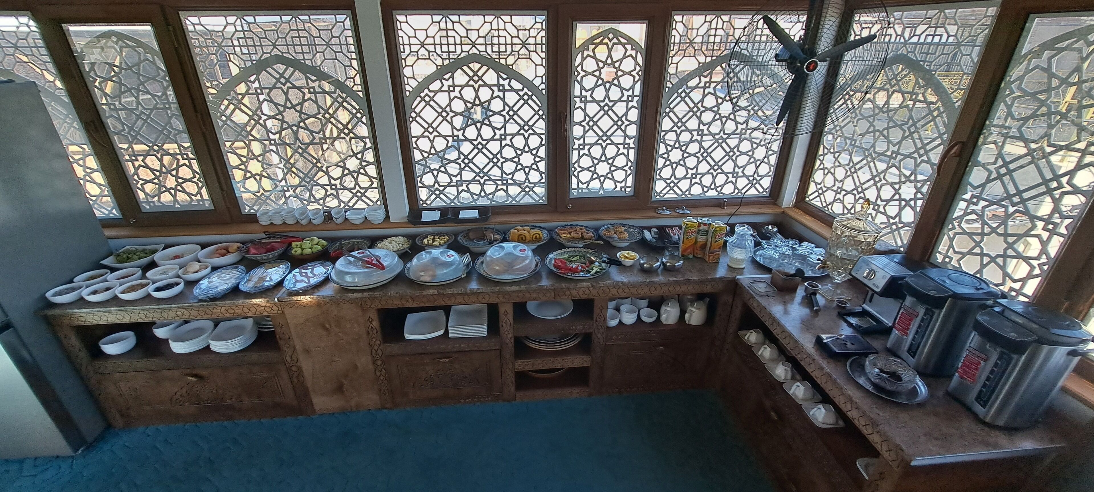 A kitchen area with a variety of dishes and utensils on the counter, a coffee machine, and a fan.