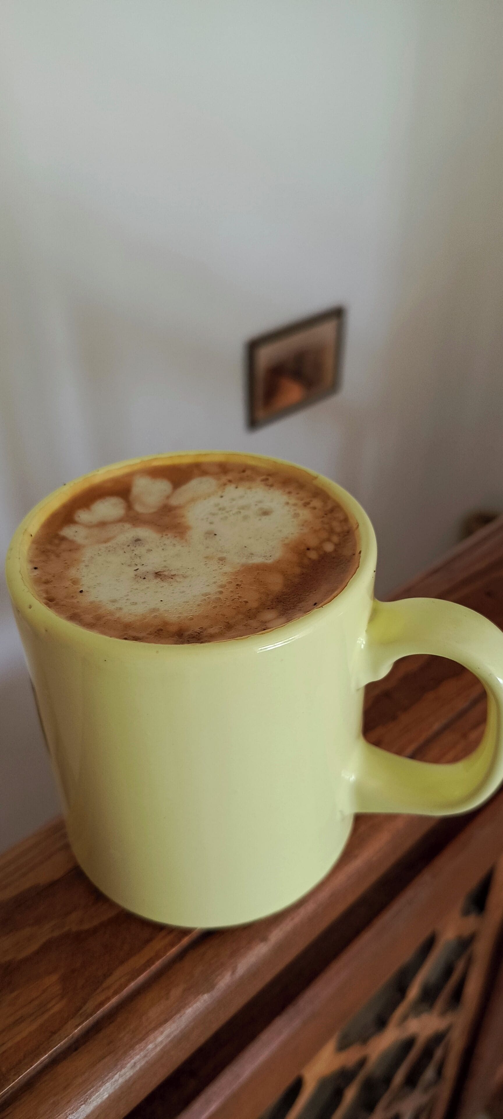 A yellow mug with a latte on a wooden table.