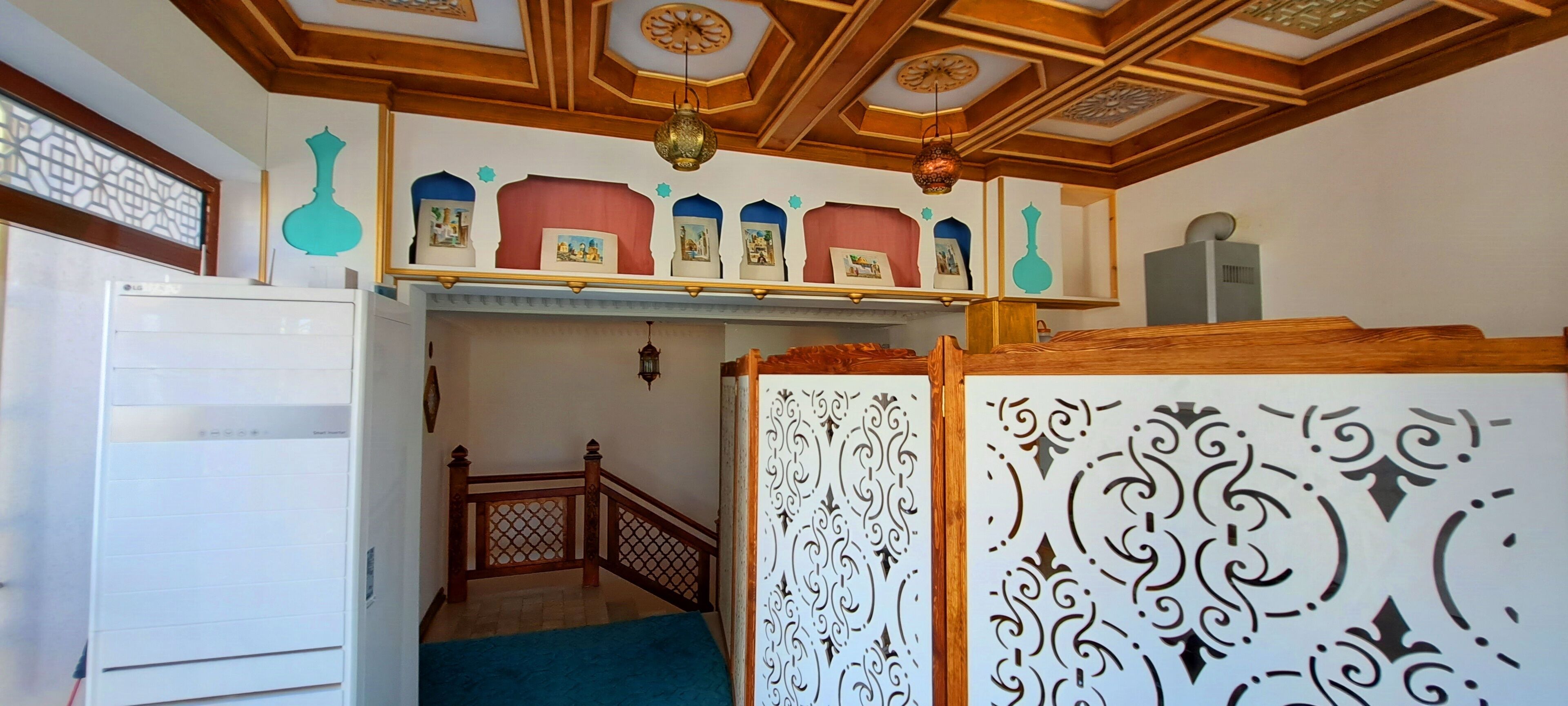 A room with a wooden ceiling, a white refrigerator, a staircase, and a decorative wall with a patterned partition.