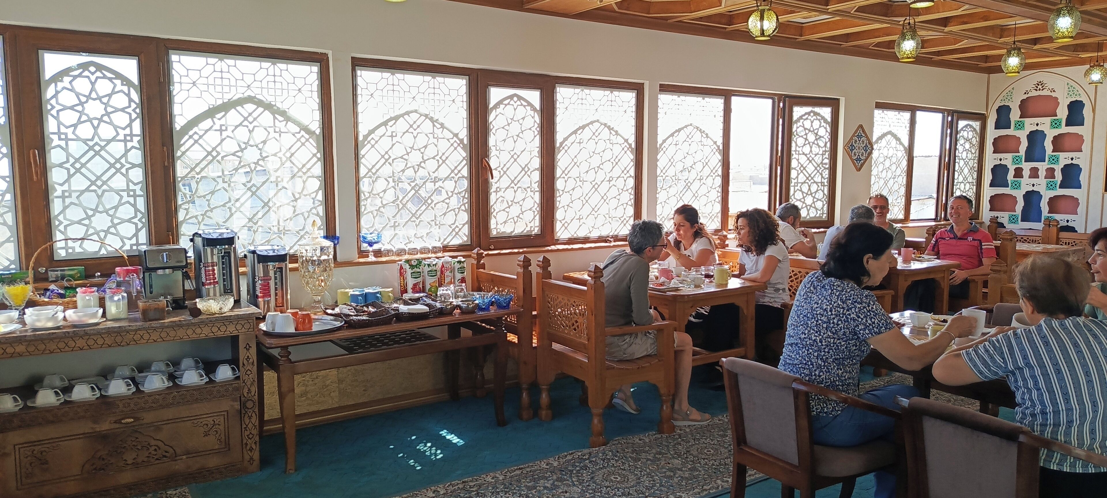 A restaurant with large windows, wooden furniture, and a variety of dishes displayed on the counter.