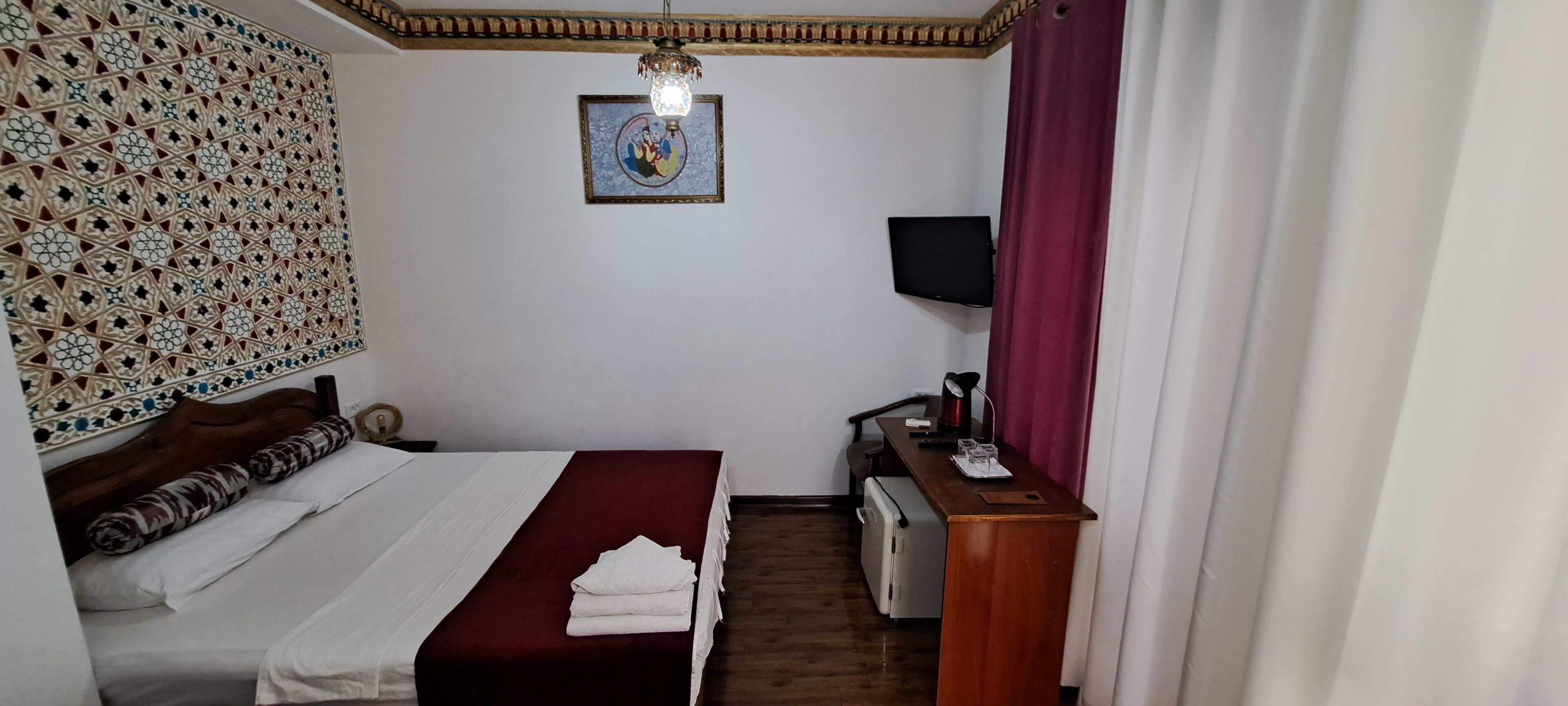 Une chambre d’hôtel équipée d’un lit, d’un bureau, d’une télévision et d’un panneau décoratif mural.