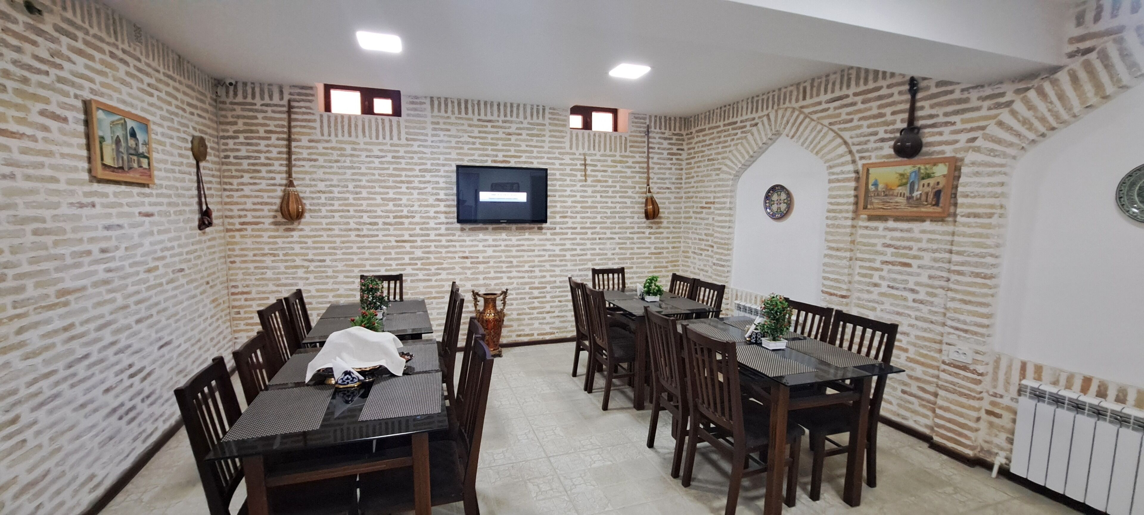 Comedor con paredes de ladrillo, una televisión de pantalla plana y mesas y sillas de madera.
