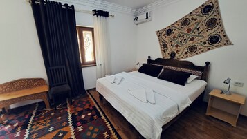 Un dormitorio con una cama, un banco, un tapete estampado y un tapiz en la pared.