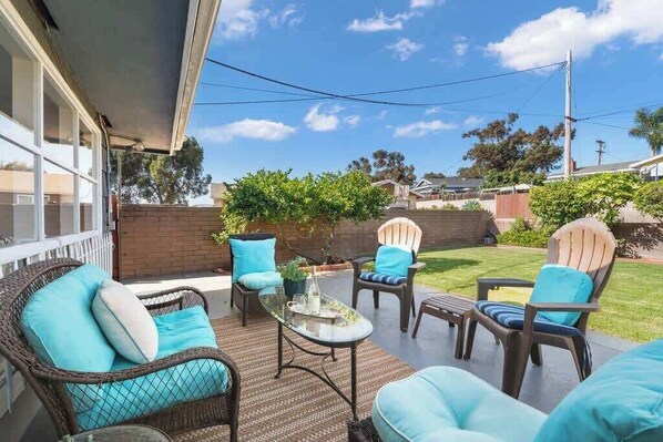 An outdoor patio with wicker furniture, a glass table, and a view of the backyard.