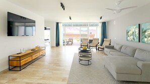 A modern living room with a flat-screen TV, a wooden TV stand, a grey sofa, and a dining area with chairs and a table. - Villa Brisa Summary: (Playa Blanca)