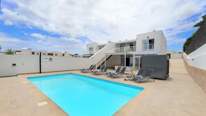 A modern pool area with a clear blue pool, sun loungers, and a two-story building with a balcony. - Villa Brisa Summary: (Playa Blanca)